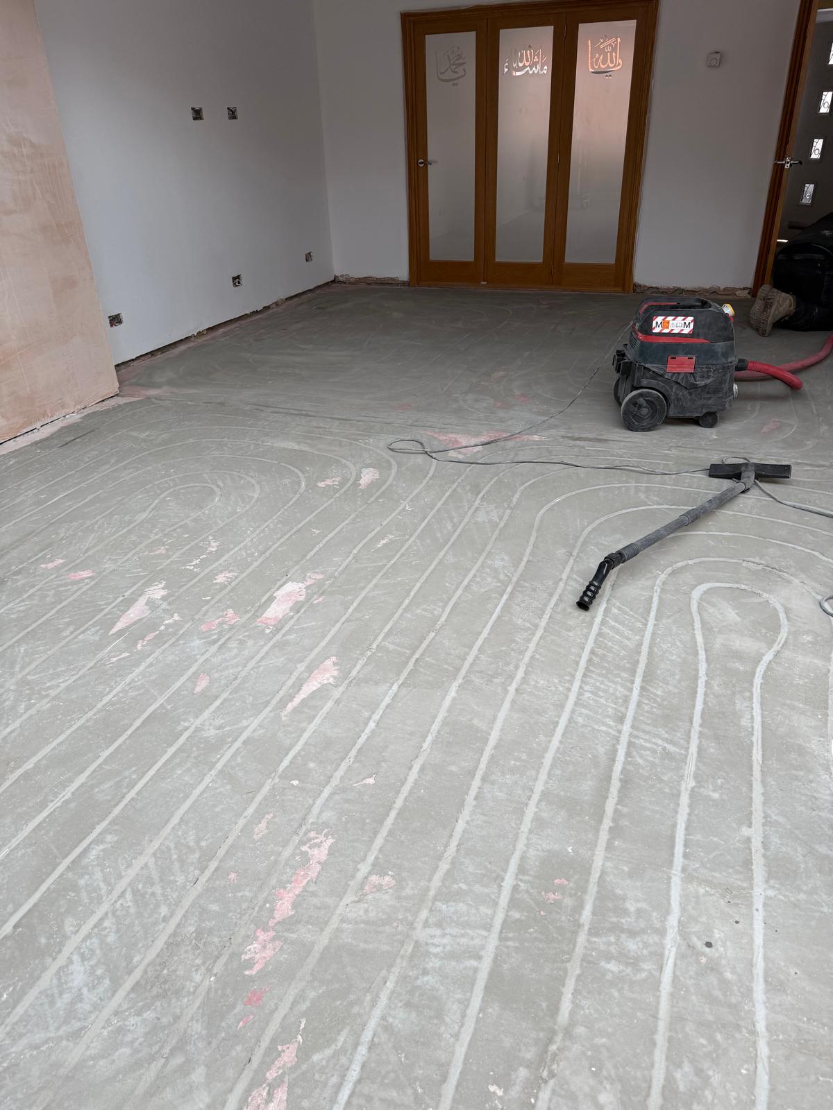 Retrofit floor milling, UFH pipe channels routed directly into an existing concrete slab with dust extraction in an occupied Cheshire home