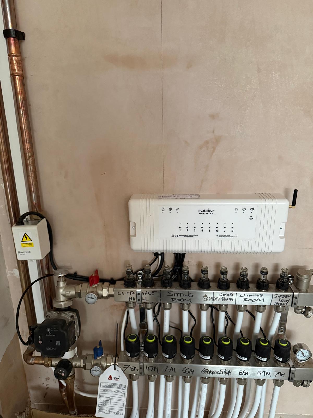 Heatmiser UH8-RF V2 smart wiring centre installed above a 9-zone stainless UFH manifold with rooms labelled per zone